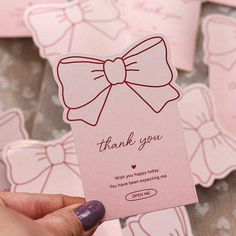 a hand holding up a pink card with a bow on it's side that says thank you