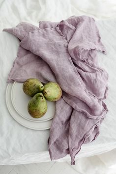 three pears on a white plate with a purple scarf draped over the table top