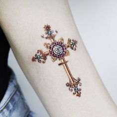 a cross tattoo on the left arm with jewels around it and an eyeball in the center