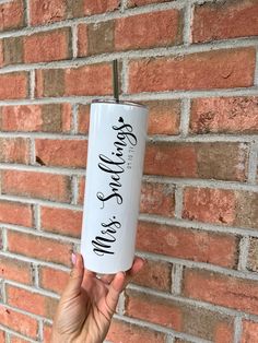 a woman holding up a white tumbler with black writing on it