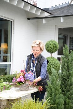 a woman is arranging flowers in front of her house with potted plants on the table