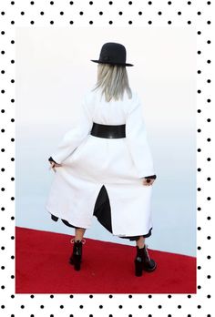 a woman in a white coat and black hat is standing on a red carpet with polka dots