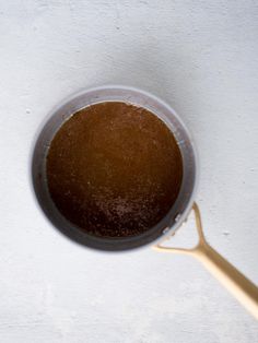 a cup filled with brown liquid sitting on top of a white counter next to a gold spoon