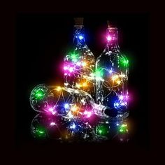 two bottles with christmas lights on them sitting next to each other in front of a black background