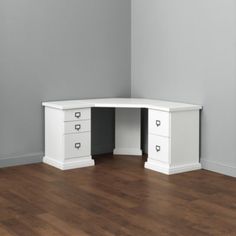 a white corner desk with two drawers on the bottom and one at the top, against a gray wall