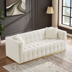 a white couch sitting on top of a wooden floor next to a lamp and window