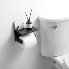 a white toilet sitting next to a roll of toilet paper on a black shelf above it