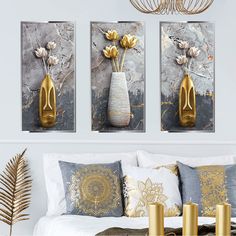 three gold vases with flowers in them on a wall next to a white bed