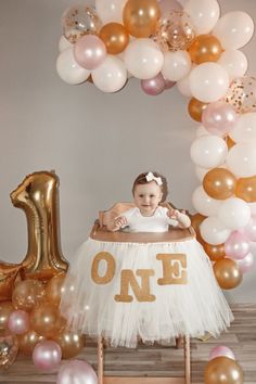 a baby sitting in a chair surrounded by balloons and streamers with the number one on it