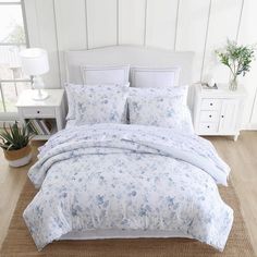 a white bed with blue flowers on it in a room next to a dresser and lamp