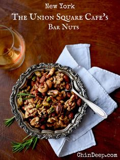 a bowl filled with nuts on top of a wooden table next to a glass of wine