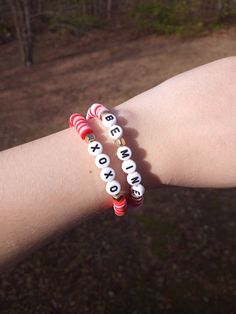 two red and white bracelets with words on them are held by someone's arm