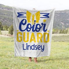 a person standing in a field holding a sign that says color guard lindsey