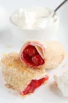 a white plate topped with two pastries covered in jelly and whipped cream next to a bowl of yogurt