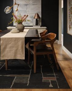 a dining room with black walls and wooden chairs, an art work on the wall