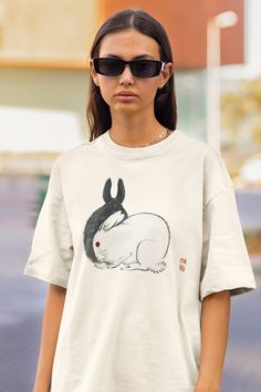 Embrace the whimsy of traditional Japanese art with our Oversized T-shirt featuring a Retro Japanese Rabbit design by Kono Bairei. This unisex drop-shoulder tee captures the gentle charm and symbolic significance of rabbits in Japanese culture, presented through the exquisite artistry of Kono Bairei. Ideal for those who appreciate the blend of historical art with modern fashion, this shirt seamlessly marries the serene beauty of nature with the dynamic edge of contemporary streetwear. ✤ Kono Bairei's Japanese Rabbit Art: Highlights a beautifully detailed rabbit design by Kono Bairei, showcasing the elegance and tranquility rabbits hold within Japanese art, offering a piece of cultural heritage in a wearable form. ✤ Comfortable Oversized Fit: The relaxed, drop-shoulder silhouette provides a Artsy Short Sleeve T-shirt With Artwork, Cotton Crew Neck T-shirt With Artwork, White Cotton Tops With Custom Artwork, White Cotton Shirt With Custom Artwork, Cotton Graphic Tee With Artwork, Graphic Tee Cotton T-shirt With Artwork, Artistic White Tops With Custom Artwork, Cotton Artwork T-shirt With Short Sleeves, Cotton Artwork T-shirt With Crew Neck