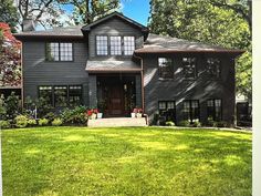 a large gray house sitting on top of a lush green field in front of trees