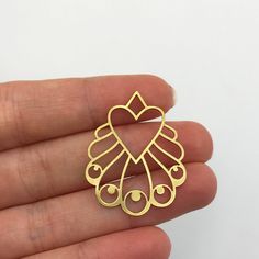 a hand holding a gold colored heart shaped brooch with hearts in the middle and two eyes on each side