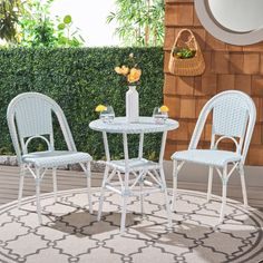 three chairs and a table on a rug in front of a brick wall with green plants