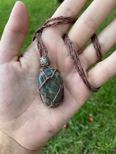 a hand holding a green stone pendant on it's string in front of some grass