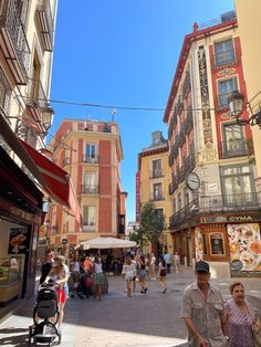 people are walking down the street in front of buildings with shops on each side and one man is pushing a stroller