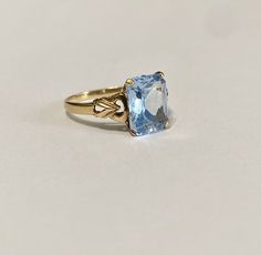 Beautiful 1940s era vintage 10k rosy yellow gold ring featuring a swiss blue topaz stone. The radiant blue topaz stone is radiant cut and secured by four prongs. The ring's shoulders are elegantly cinched with milgrain and repousse design details. Lovely piece of fine vintage jewelry, circa 1940! ERA - Circa 1940s / Retro METAL / MATERIAL - 10k gold, blue topaz MARKINGS / HISTORY - 10k SIZE / MEASUREMENTS - Size: 6 , Swiss Blue Topaz stone: approximately 10 x 8 mm, Weight: 2.15 grams, Shank: Tap Vintage Blue Topaz Ring With Prong Setting, Vintage Blue Topaz Ring For Formal Occasions, Vintage Yellow Gold Rings With Blue Topaz, Vintage Blue Topaz Ring With Diamond Cut, Vintage Yellow Gold Blue Topaz Rings, Vintage Blue Gemstone Birthstone Ring, Vintage Blue Topaz Ring In 14k Gold, Vintage Solitaire Topaz Ring, Vintage 14k Gold Topaz Birthstone Ring