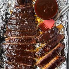 bbq ribs and barbecue sauce on tin foil with tongs next to the grill