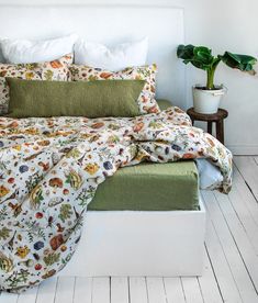 a bed with green and white sheets, pillows and blankets on top of it next to a potted plant