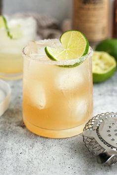 a close up of a drink on a table with limes and bottles in the background