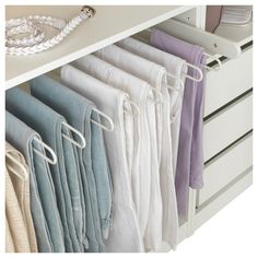 an organized closet with clothes hanging on hooks and white drawers, along with other items