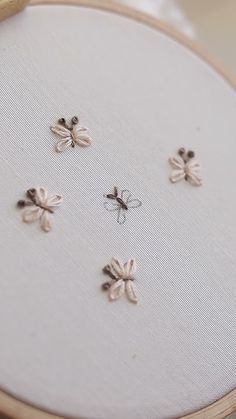 four embroidered bugs sitting on top of a white piece of cloth in front of a wooden frame