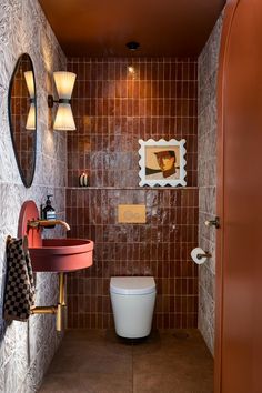 a bathroom with a toilet, sink and mirror in it's corner area next to a tiled wall