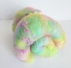 a green and pink colored yarn with sprinkles on the end, sitting on a white surface