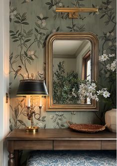 a table with a mirror and lamp on it next to a wallpapered wall