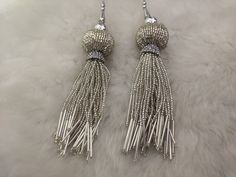 two pairs of silver colored earrings with beads and tassels on white furnishing