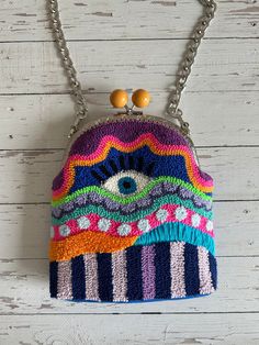 a multicolored purse hanging from a chain on a white wooden background with beads