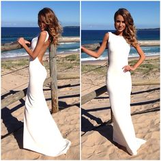 a beautiful woman in a white dress posing on the beach with her hands on her hips