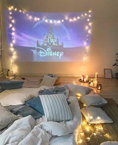 a bed with lots of pillows and lights on the headboard, in front of a projection screen