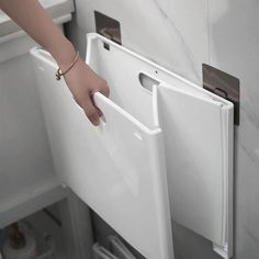 a person's hand is on the door handle of a white toilet paper dispenser