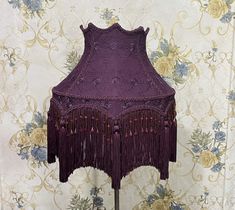 a purple lamp shade with fringes on a wooden stand in front of a floral wallpaper