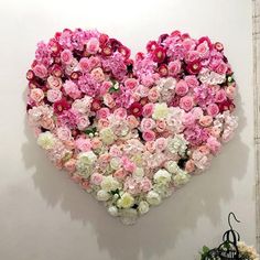 a heart - shaped arrangement of pink and white flowers hangs on the wall in front of a mirror