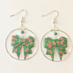 a pair of earrings with green and pink bows on the front, hanging from silver hoops