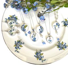 a white plate topped with blue flowers next to a bunch of necklaces on top of it