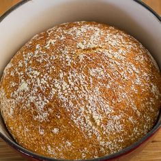 a round loaf of bread in a red and white pan on a wooden table top