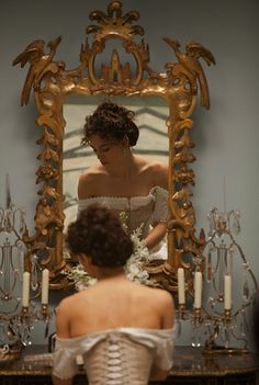 a woman in front of a mirror with candles on the table and another person looking at her reflection