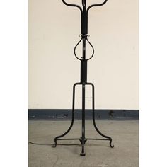 a black metal floor lamp sitting on top of a cement floor next to a white wall