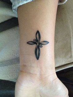 a cross tattoo on the wrist is shown in black ink, with an intricate design