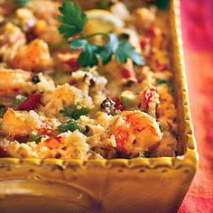 a casserole dish with shrimp and vegetables in it on a red tablecloth