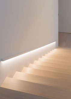 an empty room with white walls and wooden flooring is lit by led lighting on the wall