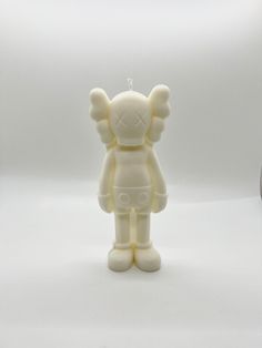 a small white teddy bear with wings on it's head and eyes, standing next to a clock